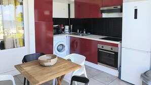 Eine kleine Küche mit roten und weißen Schränken, einer Waschmaschine, einem Herd und einem Deckenventilator.