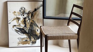 Ein Zimmer mit einem gerahmten abstrakten Gemälde, einem gewebten Sessel und einem gemusterten Teppich.