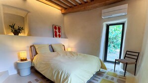 Ein Schlafzimmer mit Bett, Nachttischlampen, einem Sessel, einem Fenster und einer Klimaanlage.