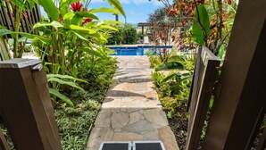 A stone pathway leading to a pool surrounded by lush tropical plants.