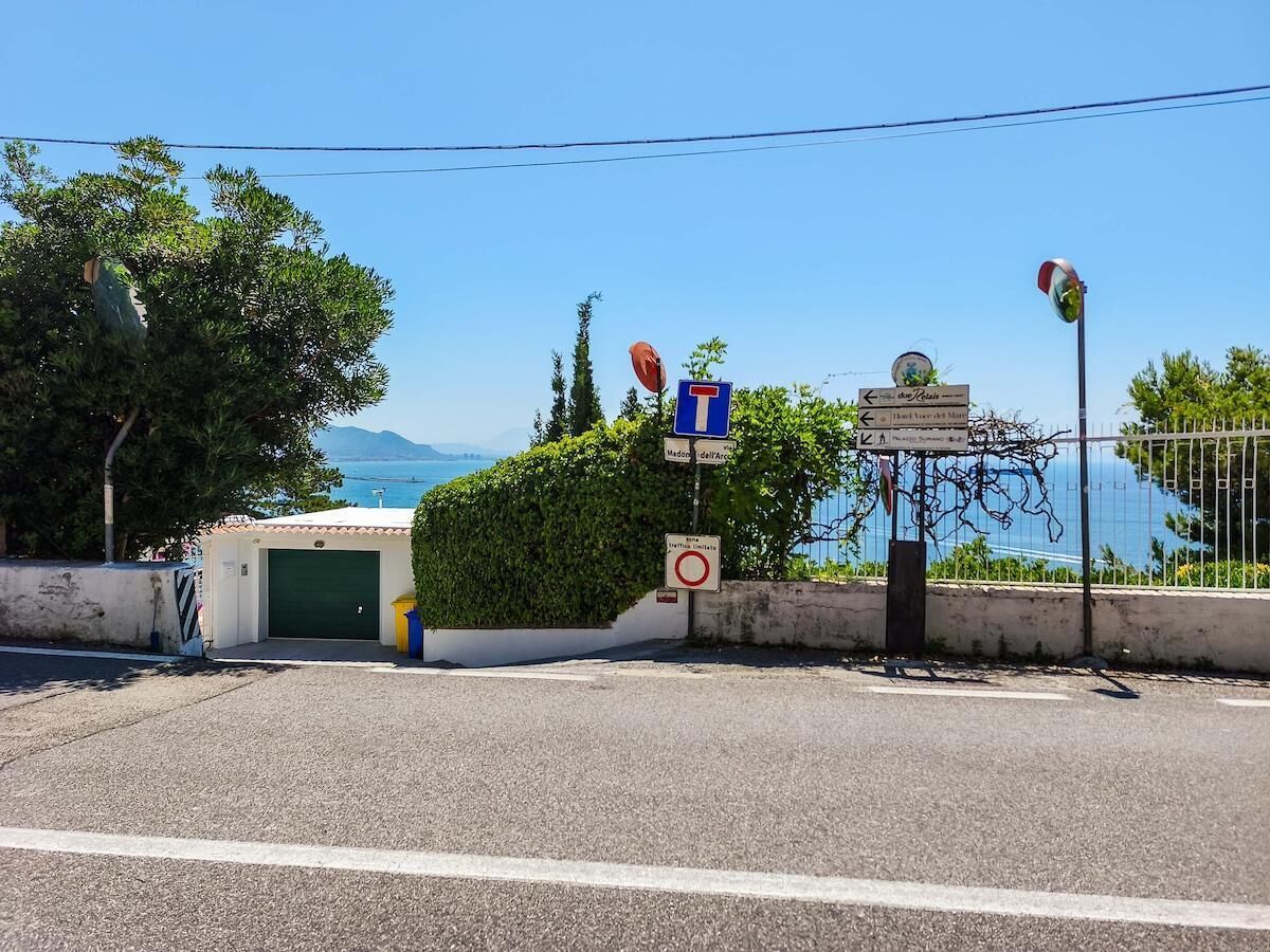 Una carretera costera con una verja verde, indicaciones y vistas al mar.
