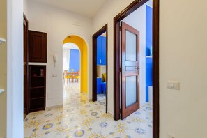 Un pasillo con suelo de baldosas, armarios de madera y una puerta que da a una habitación con pared azul.