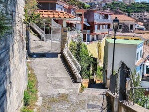 Una estrecha escalera de piedra conduce a una entrada con reja, rodeada de edificios con tejados de teja.