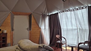 A tent-style room with a bed, a chair, a table, and a door.