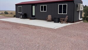 Ein einstöckiges Gebäude mit rotem Dach, einer Beton-Terrasse und zwei Holzstühlen.
