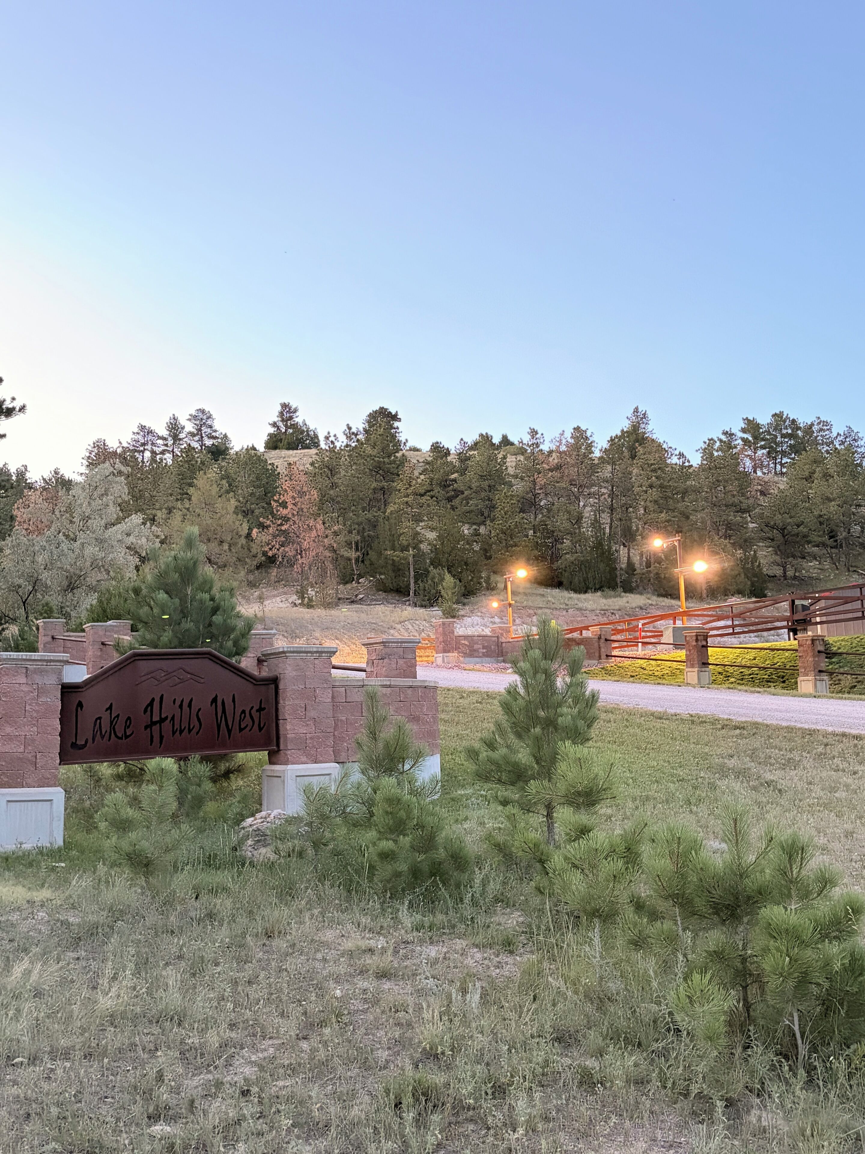 A sign for Lake Hills West with a brick wall and a grassy area in front.