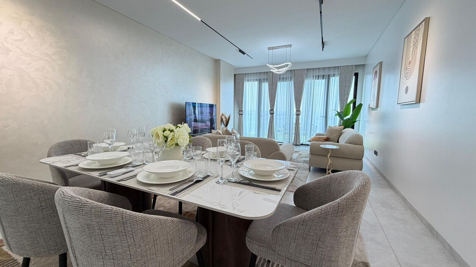 Un comedor moderno con una mesa preparada para cuatro personas, un sofá y una televisión al fondo.