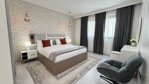 A modern bedroom with a large bed, bedside tables, a chair, and a view of the outdoors.