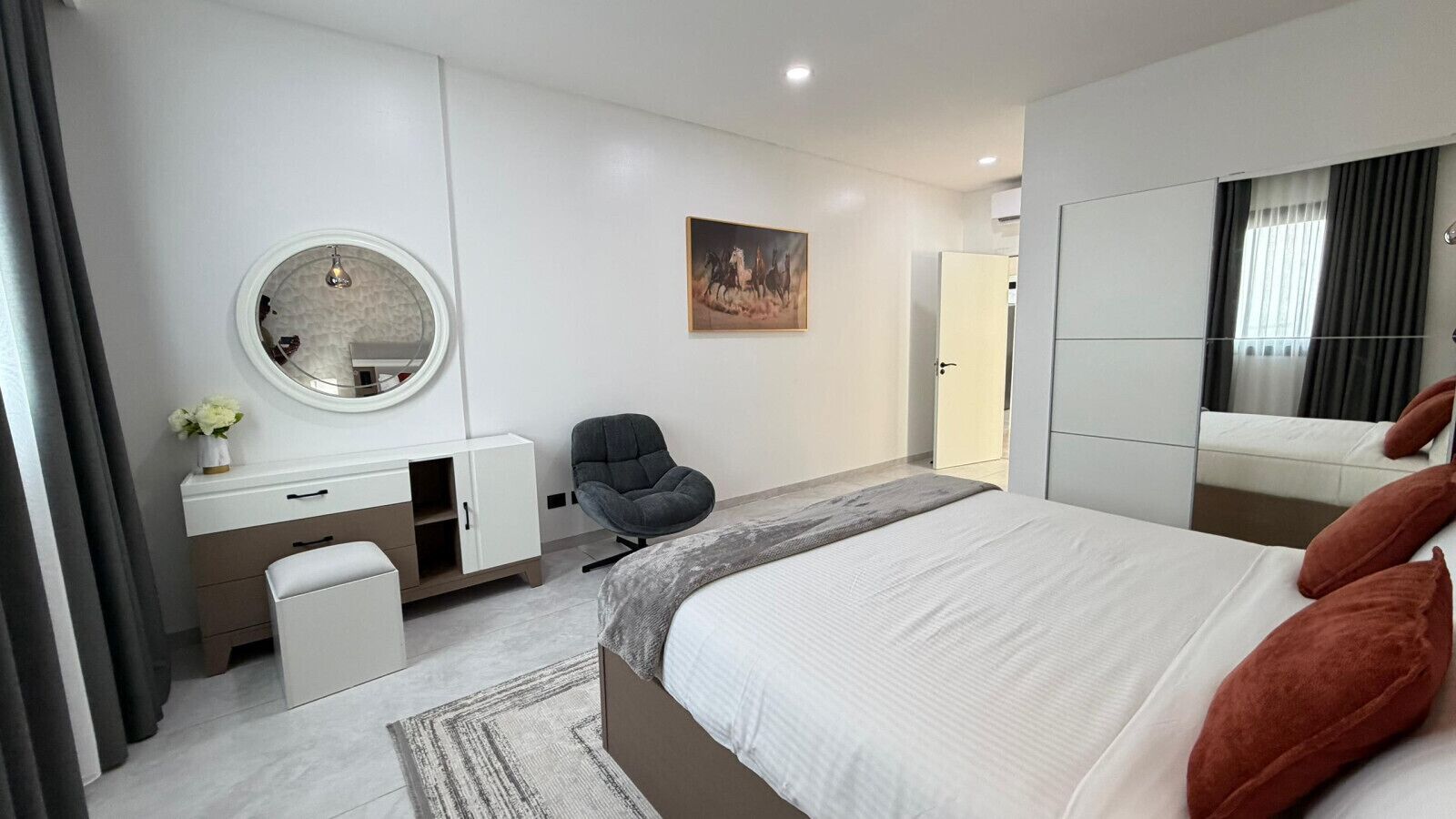 Een moderne slaapkamer met een bed, een bureau, een stoel, een spiegel en een schilderij aan de muur.