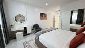 A modern bedroom with a bed, a desk, a chair, a mirror, and a painting on the wall. - Stunning River View 2 BDR Apartment in Gombe (Kinshasa)