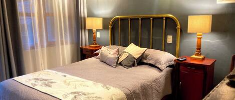 A neatly made bed with a patterned bedspread, two bedside lamps, a nightstand, and a chair.
