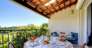 Een balkon met een ontbijttafel, compleet met croissants, fruit en drankjes.