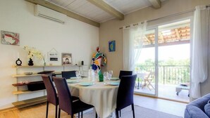 En spiseplads med et bord dækket til fire personer, en person står ved vinduet, og en balkon med udsigt.