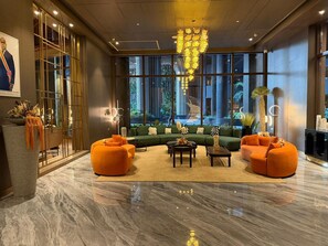 A modern lobby with a marble floor, green sofas, orange armchairs, and a large chandelier.