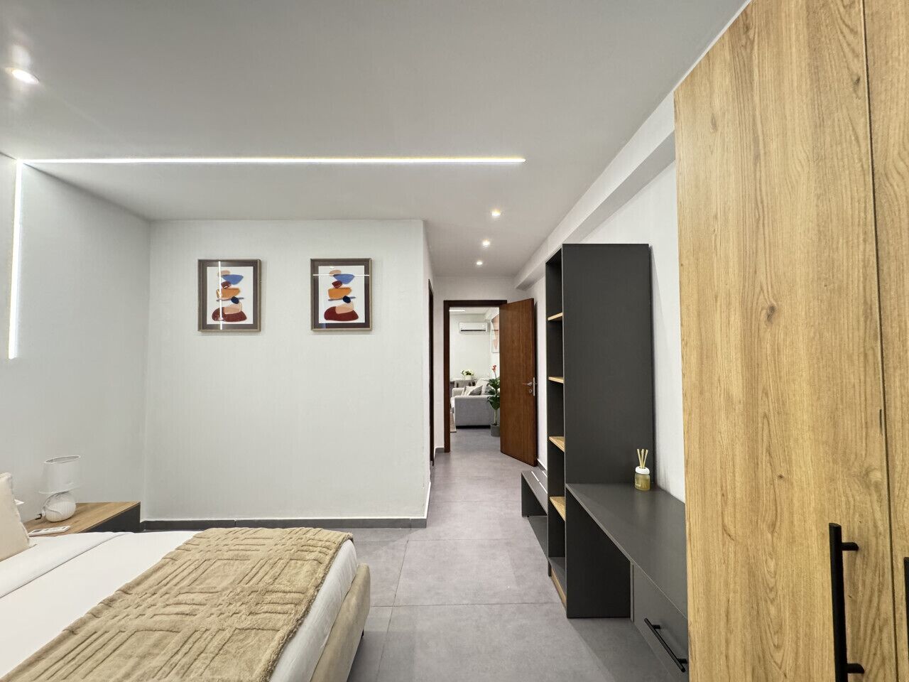 A modern bedroom with a bed, bedside tables, a wardrobe, and a hallway leading to a living area.