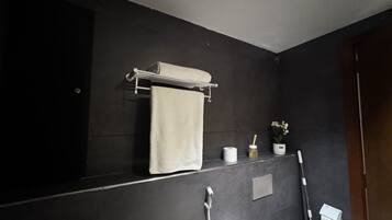Een badkamer met een handdoek aan een rek, een toiletpapierhouder en een handdroger.