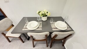 A dining table set for two with white plates, glasses, and a vase of flowers.