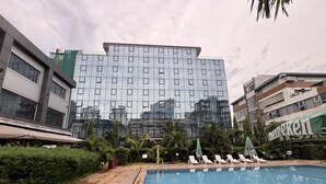 A swimming pool with lounge chairs and umbrellas, surrounded by greenery and modern buildings.