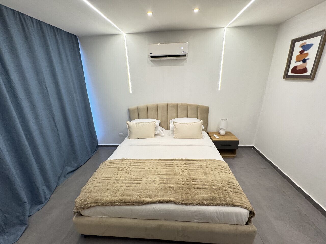 A modern bedroom with a bed, bedside tables, an air conditioning unit, and a curtain.