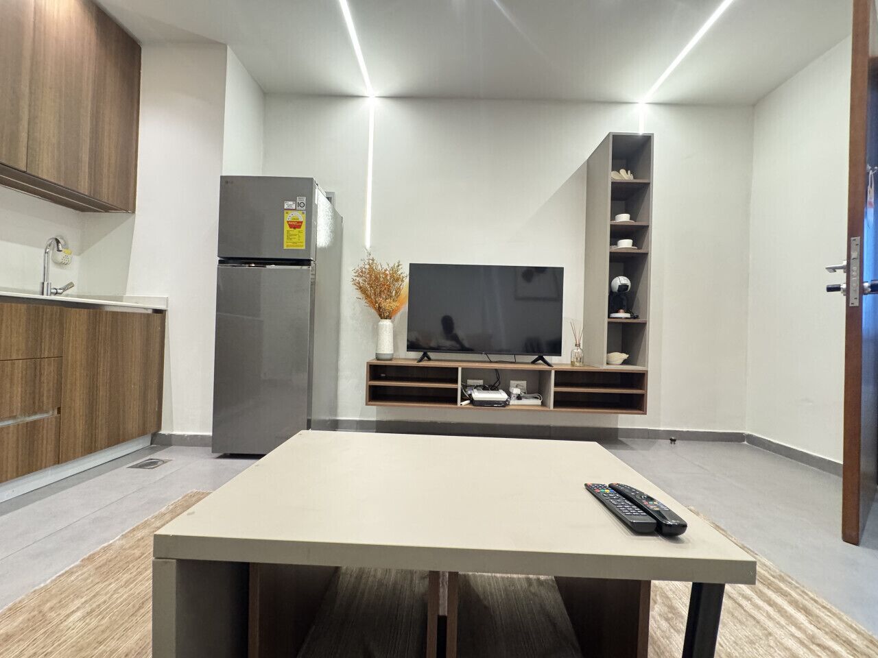 A modern living room with a flat-screen TV, a dining table, and a built-in kitchen area.