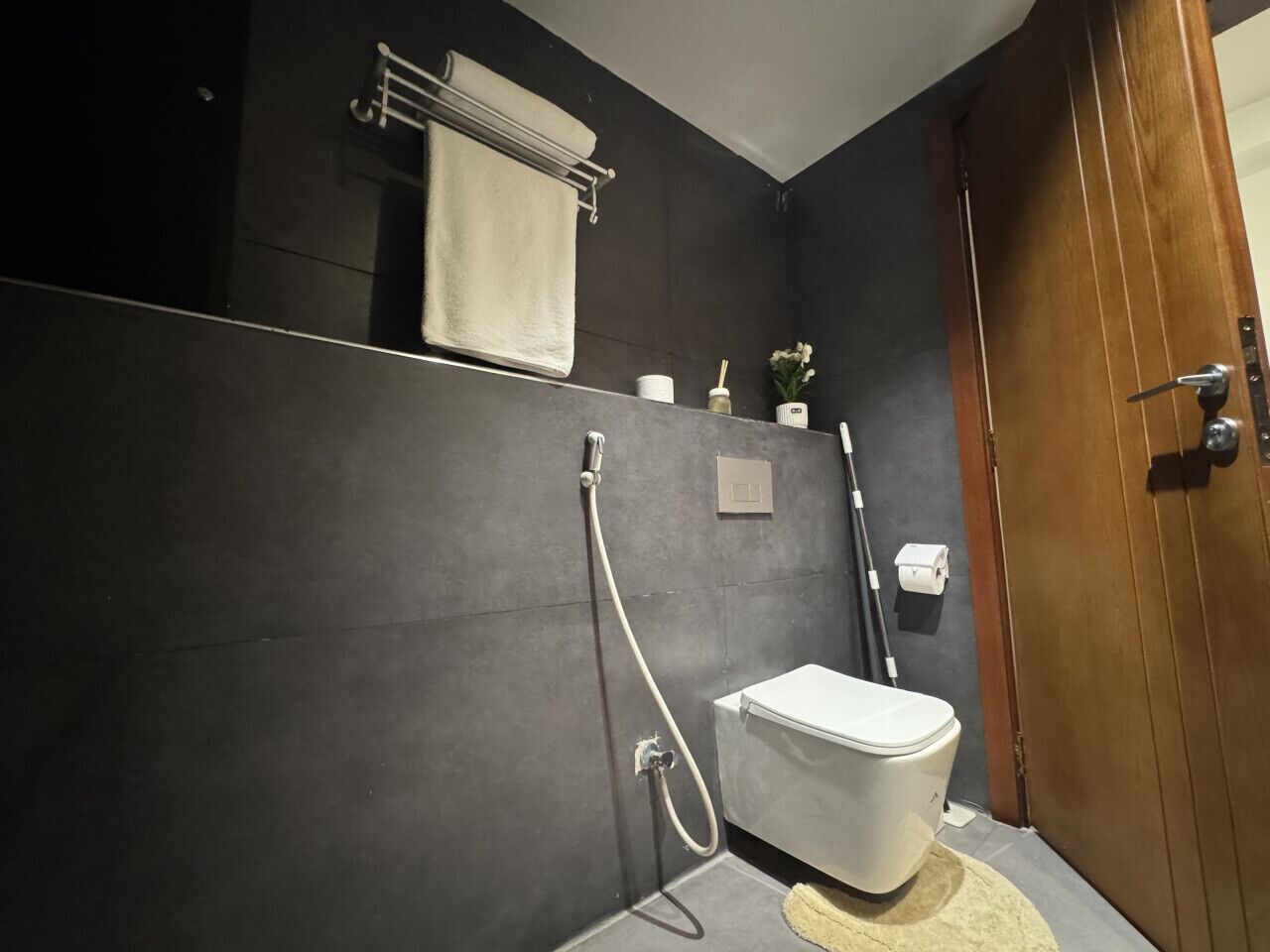 Et badeværelse med toilet, brusebad, håndklædestige og en trædør.