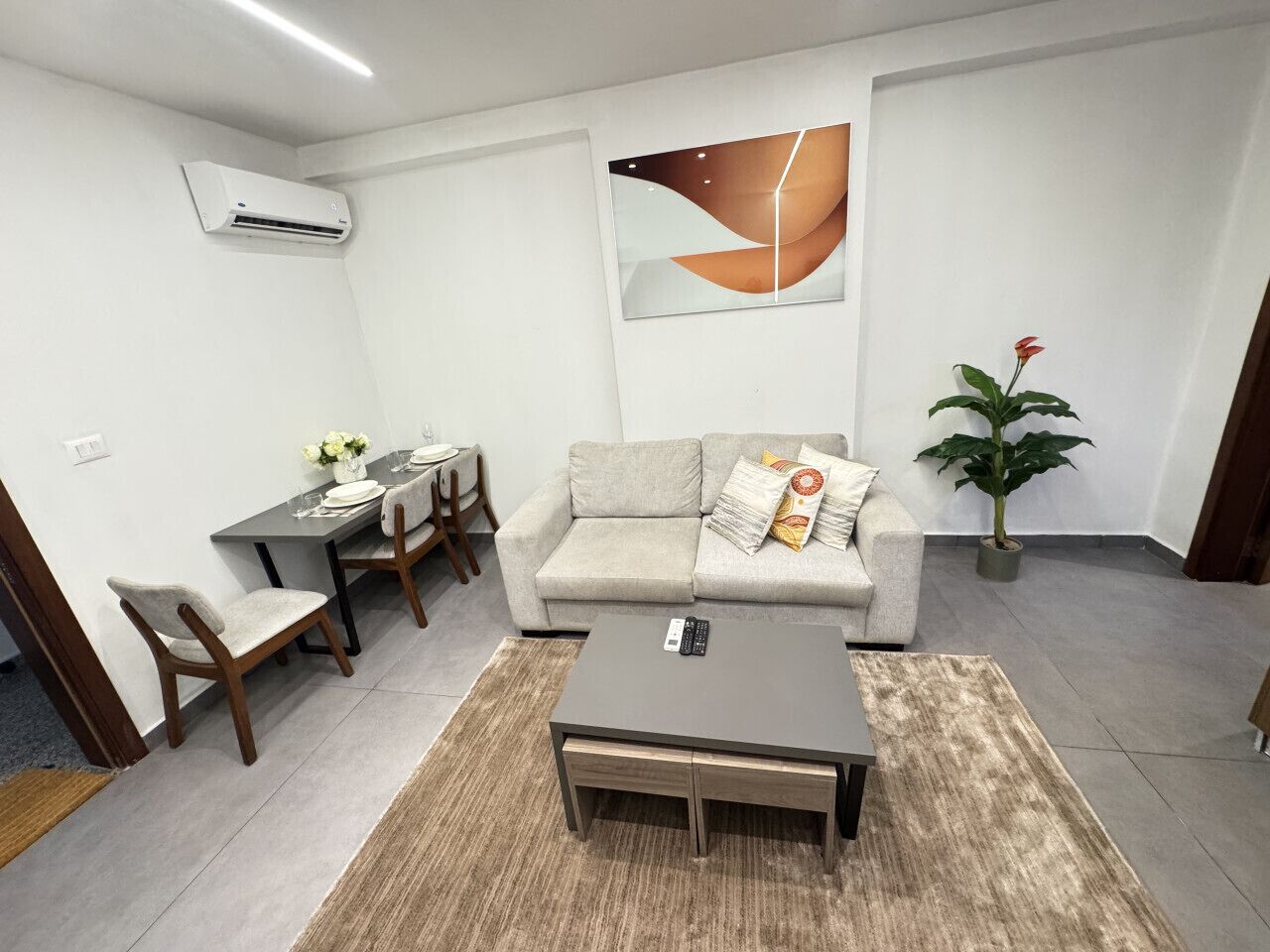 Een moderne woonkamer met een bank, salontafel, eettafel, stoelen en een potplant.