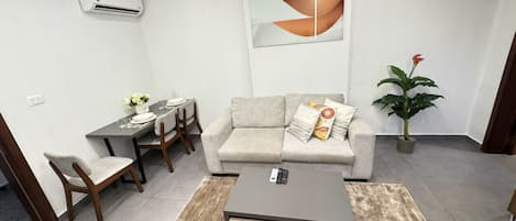 Een moderne woonkamer met een bank, salontafel, eettafel, stoelen en een potplant.