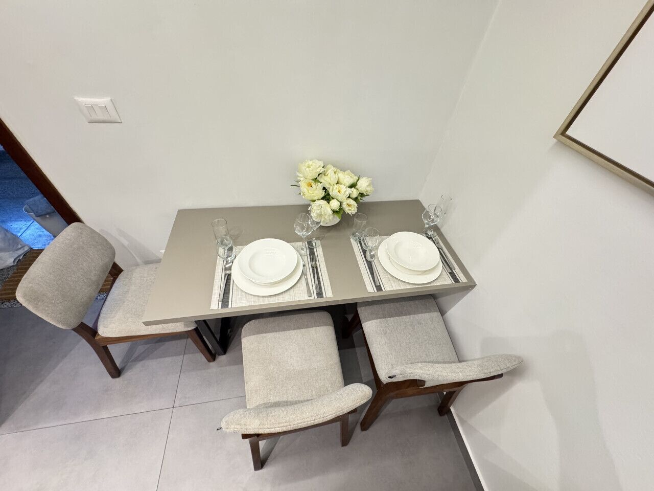 Een eethoek met een tafel gedekt voor twee personen, inclusief borden, bestek en glazen.
