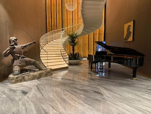 Eine prächtige Lobby mit Marmorboden, einem Flügel, einer Wendeltreppe und einer Kriegerstatue.
