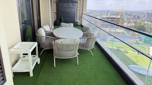 Un balcón con césped artificial, mobiliario de mimbre y vistas a un paisaje urbano.