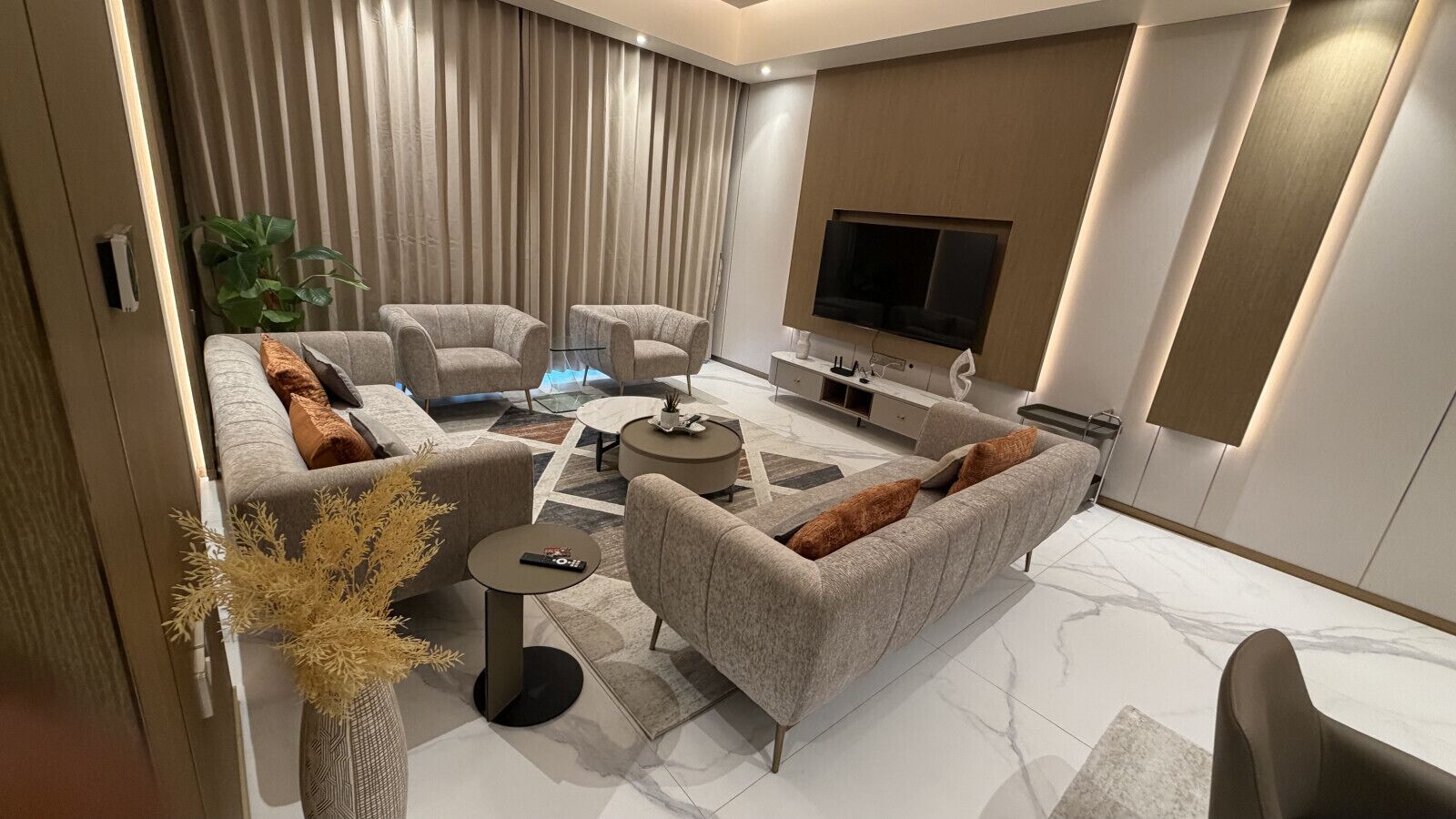 A modern living room with a sofa set, a coffee table, and a flat-screen TV mounted on the wall.
