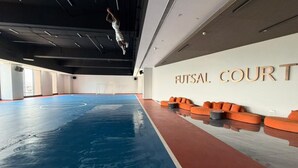 Ein Innenbereich-Sportfeld mit blauem Boden, orangefarbenen Sitzplätzen und einer Wand mit dem Schriftzug 'HUTSAL COURT'.