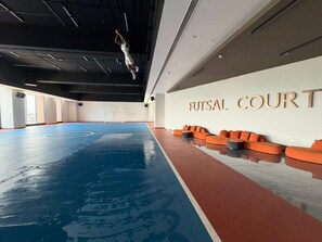 An indoor sports court with a blue floor, orange seating, and a wall with 'HUTSAL COURT' text. - Grand Résidence, 2 Bedrooms Stylish Apartment  Kinshasa (Gombe) – Galerie Lafontaine (Kinshasa)