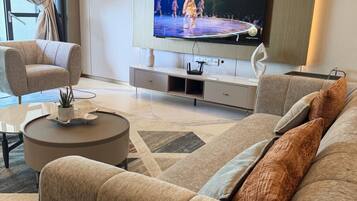 A modern living room with a flat-screen TV mounted on the wall, a beige sofa, a coffee table, and a patterned rug.