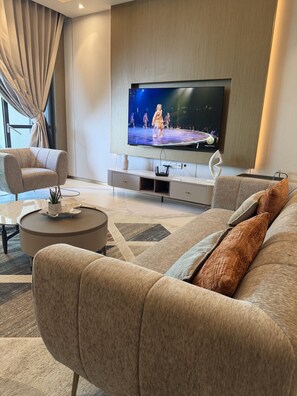 A modern living room with a flat-screen TV mounted on the wall, a beige sofa, a coffee table, and a patterned rug.