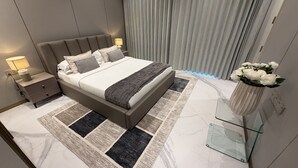 Ein modernes Schlafzimmer mit einem großen Bett, Nachttischen, einem Glastisch und einer Vase mit Blumen.