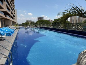 Una piscina con agua azul cristalina, rodeada por una terraza de madera y sillones de descanso.