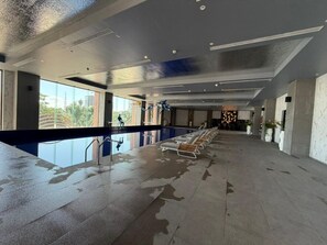 A spacious indoor area with a long bench along the wall, a pool with a clear view of the outdoors, and a modern ceiling design.