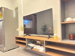 A modern living room with a flat-screen TV on a wooden stand, a refrigerator, and a shelf with decorative items. - Modern & Cosy Oasis in Central Gombe – Pool, Spa & (Kinshasa)