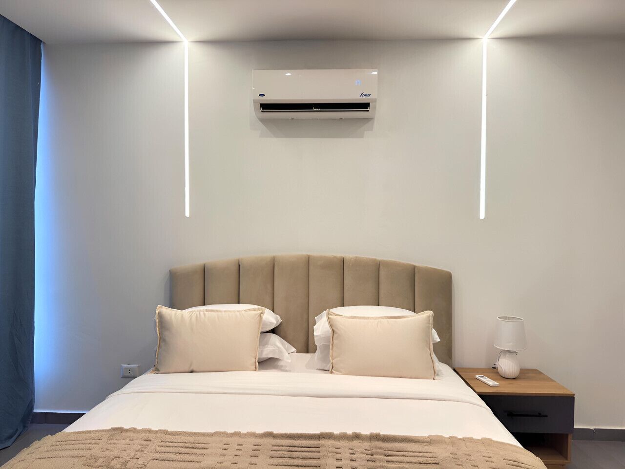 Een hotelkamer met een bed, nachtkastje, lamp en een airconditioning.