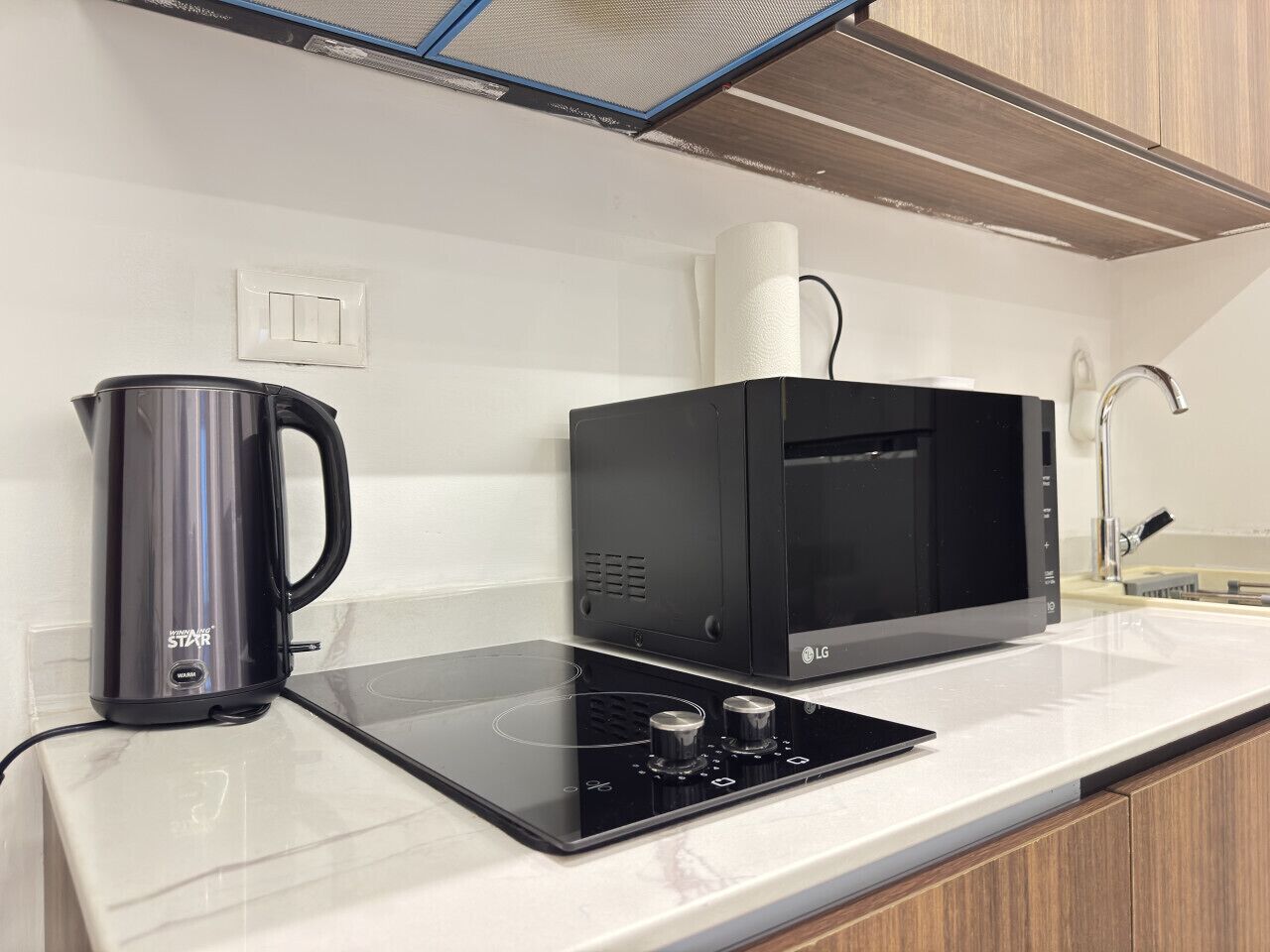 Een keuken met een zwarte magnetron, een waterkoker en een glazen kookplaat.