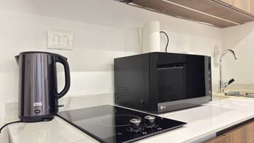 Een keuken met een zwarte magnetron, een waterkoker en een glazen kookplaat.