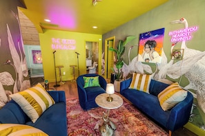 Una habitación vibrante con dos sofás azules, una mesa redonda y un letrero de neón que dice 'THE GLED BUNGALOW'.