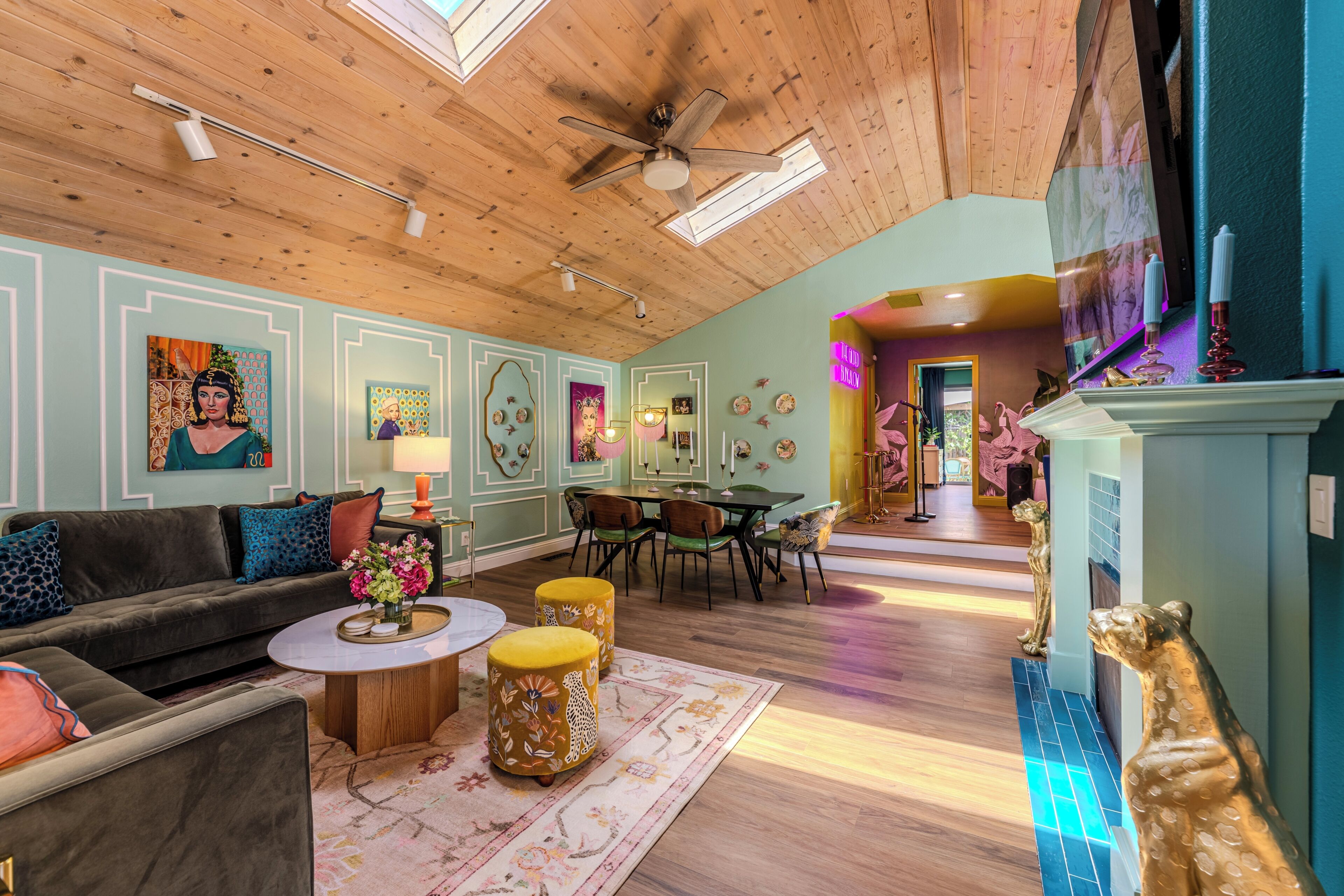 Une pièce avec un plafond en bois, un ventilateur de plafond, un canapé, une table à manger avec des chaises et un mur décoratif orné d’œuvres d’art.