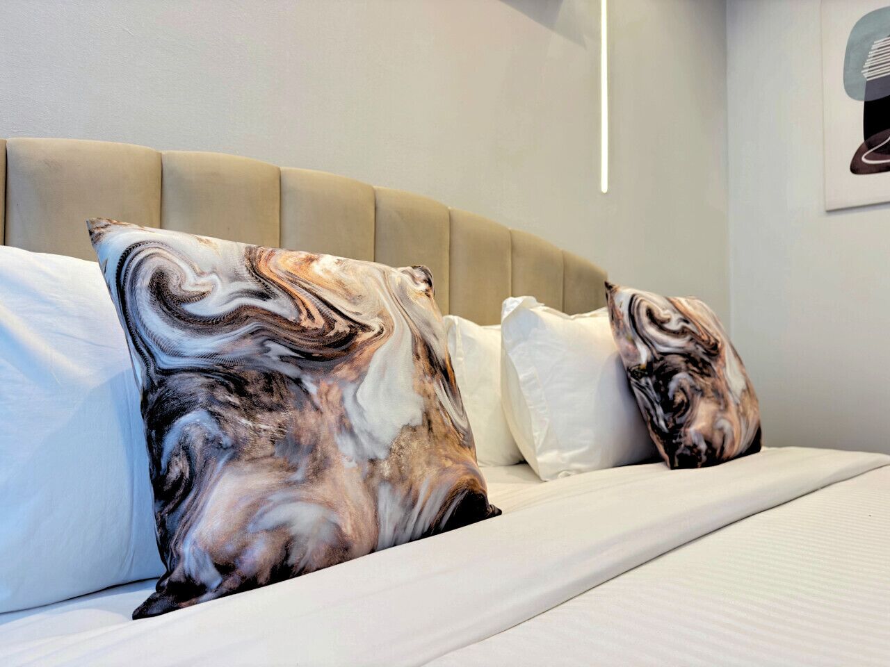 Una cama con cabecera, almohadas y una lámpara fijada a la pared.