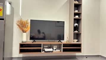 A modern living room with a flat-screen TV mounted on a wooden console, a built-in shelf unit, and a decorative vase with dried flowers.
