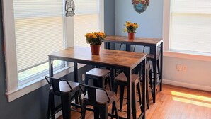A dining area with a wooden table and black chairs, large windows with blinds, and a wall-mounted decorative item. - Green Little Havana (Miami)