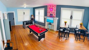 A room with a pool table, a foosball table, a television, and a dining area with chairs and a table. - Green Little Havana (Miami)