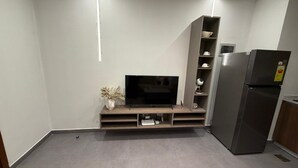 A compact living space with a flat-screen TV on a wooden stand, a built-in shelf unit, a refrigerator, and a small potted plant. - Cozy 1 bedroom Studio Apartment with Pool in Gombe (Kinshasa)