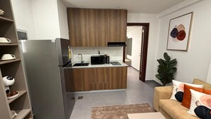 A compact kitchen with a refrigerator, microwave, and wooden cabinets. - Cozy 1 bedroom Studio Apartment with Pool in Gombe (Kinshasa)
